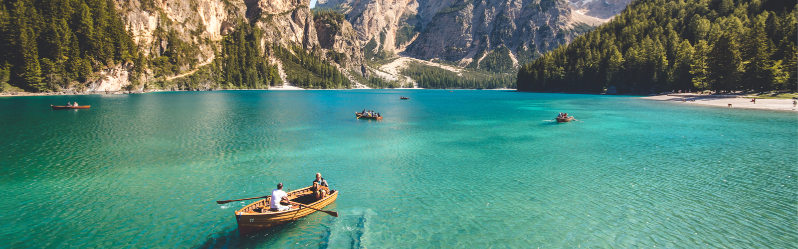Five boats spread across a clear blue lake surrounded by mountains and evergreen trees.